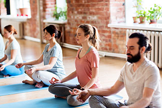 Die richtige Yoga-Kleidung: Eine Gruppe von jungen Leuten sitzt meditierend auf ihren Yogamatten in einer Reihe.