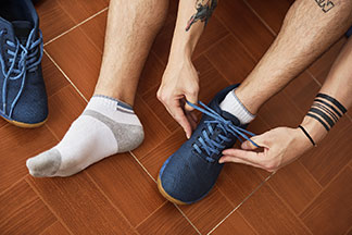 Nahaufnahme von den Füsse eines Mannes, der Sportsocken mit verstärkter Fersen- und Ballenpartien trägt, einen Schuh bereits an hat und diesen bindet.