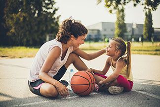 Mutter und Tochter sitzen sich gegenüber am Boden und machen eine Pause vom Basketballspielen.