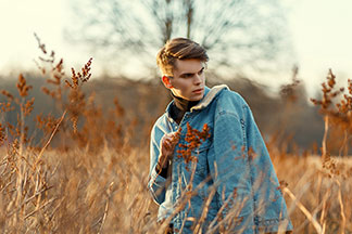 Jacke für die Freizeit: Ein junger Mann geht bei Abendstimmung durch ein herbstliches Feld, dabei trägt er seine Jeansjacke mit weissem Wollkragen über der Schulter.