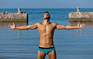 Ein junger Mann, der eine enge Herren-Badehose und eine Schwimmbrille trägt, zieht im Schwimmbad seine Bahnen mit dem Kopf unter Wasser.