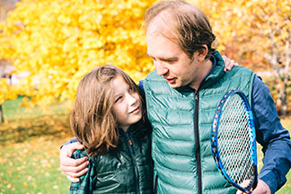 Herrenwesten für Klein und Gross: Vater und Sohn stehen Arm in Arm mit einem Tennisschläger in der Hand in der Natur.