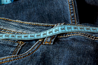 Nahaufnahme einer Jeans und eines Massbandes entlang des Hosenbundes.