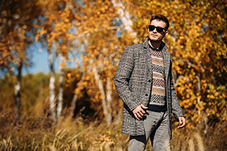 Ein junger Mann mit Sonnenbrille und kariertem Kurzmantel spaziert durch den herbstlichen Wald.