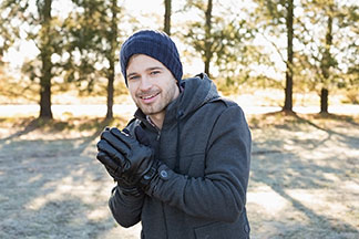 Beste Qualität für Ihre Herren-Handschuhe: Ein junger Mann, der eine blaue Wollmütze auf dem Kopf hat, reibt sich seine Hände, an denen er schwarze Handschuhe trägt, dabei lacht er in die Kamera.
