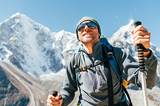 Sportaccessoires für draussen: Ein sportlicher, junger Mann wandert im Hochgebirge mit Wanderstöcken. Dazu trägt er eine Sonnenbrille sowie eine Wollmütze.