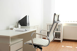 Moderner, ergonomischer Bürostuhl mit weisser Sitzfläche steht an einem weissen Schreibtisch.