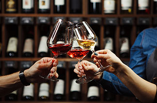 Für jeden Wein das ideal Glas: Verschiedenen Weingläsern beim Anstossen vor einem Weinregal.