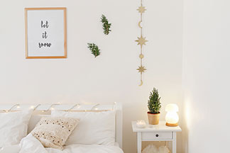Lampen in Tchibo-Qualität: Ein weiss eingerichtetes Schlafzimmer mit einem Bett und einem Nachttisch, auf dem eine angeschaltete, pilzförmige Dekoleuchte steht.