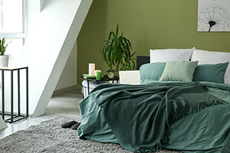 Bettwäsche für jede Jahreszeit: Ein helles Schlafzimmer mit grünen Pflanzen und einem Doppelbett, das mit weisser Bettwäsche mit einem grünen Rankenmuster überzogen ist.