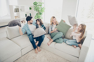 Platz für die ganze Familie: Ein Elternpaar sitzt mit ihren zwei Kindern auf einem weissen gemütlichen Big Sofa.