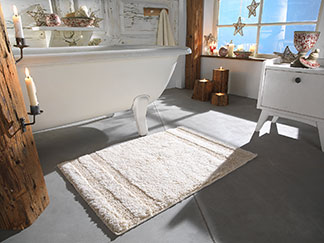 Die richtige Form finden: Ein rechteckiger weisser Badteppich liegt vor einer freistehenden Badewanne im Badezimmer.