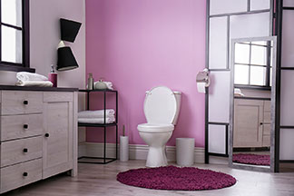 Wohltat für die Füsse: Ein violetter, runder Badteppich liegt vor der Toilette in einem modern eingerichteten Bad mit einer rosa Wand.