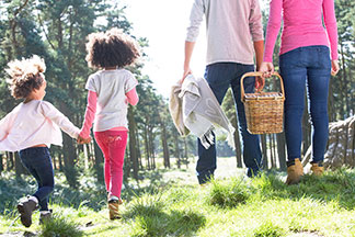 Gut gerüstet für ein Picknick: Eine junge Familie mit zwei Kindern und Picknickkorb unterwegs in der Natur.
