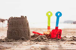 Viel Spass mit Spielzeug für draussen: Eine Sandburg am Strand neben der zwei kleine Plastikschaufeln im Sand stecken.