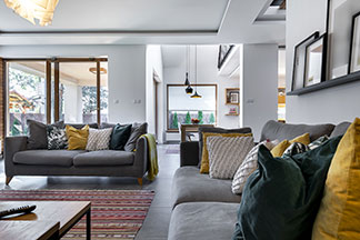 Wohnliche Atmosphäre: Ein grosses Wohnzimmer mit einem bunten Teppich und zwei grauen Sofas, die mit vielen bunten Kissen dekoriert sind.