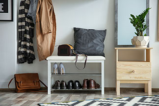 Praktisch und dekorativ: Eine weisse Schuhbank mit Schuhen steht in einem Flur mit einem Spiegel, hängenden Jacken an einer Garderobe und einem Teppich.