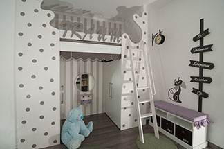 Stauraum und Sitzfläche: Ein weisses Lowboard, das im Kinderzimmer an der Wand steht, im unteren Bereich Schubfächer mit Kästen und eine lila Sitzauflage hat.