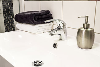 Badaccessoires in schickem Design: Ein bauchiger metallener Seifenspender steht auf dem weissen Waschbeckenrand.