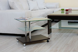 Bei Tchibo erhalten Sie qualitativ hochwertige Beistelltische: Ein Wohnzimmer mit einer weissen Couch und einem rechteckigen Beistelltisch aus Glas, der auf Rollen steht.