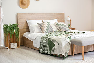 Viel Platz im Bett: In einem grossen Bett, das mit grauer Bettwäsche bezogen ist, liegen lachende, junge Eltern – zwischen ihnen ihr Kleinkind.