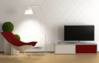 In einem Wohnzimmer steht ein rot-weisses Lowboard auf dem ein Fernseher steht, dazu ein Sessel mit rotem Bezug und eine Stehlampe.