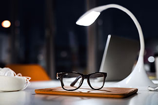 Licht beim Arbeiten: Eine weisse Bürolampe beleuchtet bei Dunkelheit den Schreibtisch.