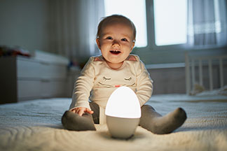 Sicheres Schlafen: Ein Baby betrachtet aus seinem weissen Gitterbett neugierig die Umgebung.