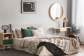 Ein grosses Bett mit Dekokissen im Schlafzimmer und mit einem grossen, runden Spiegel als Deko an der Wand.