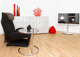 Beistelltische sind nicht nur praktisch: Ein Wohnzimmer mit einem weissen Sideboard, einem schwarzen Sessel, einem Fernseher und einem runden Beistelltisch.