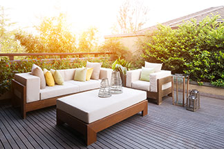 Gartenmöbel sorgen für Gemütlichkeit: Auf einer Holzterrasse stehen Loungemöbel mit hölzernen Füssen und weissen Sitzauflagen sowie verschiedene Dekokissen.