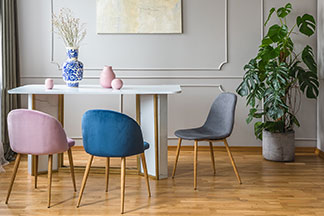 Stylische Form: An einem rechteckigen, weissen Tisch stehen drei schalenförmige Esszimmerstühle ohne Armlehnen in pink, blau und grau.