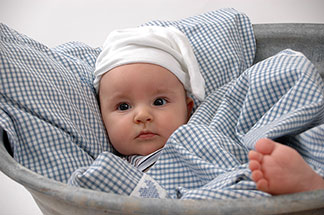 Ein Baby liegt in blau/weiß karierter Bettwäsche.